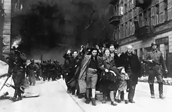 IPN copy #7Forcibly pulled out of bunkersCaptured Jews are led by Waffen SS soldiers to Umschlagplatz. In the back Nowolipie 62 & 63. See file page for possible identity of depicted people. The SS man at right has the "Totenkopf" Insignia on his collar.
